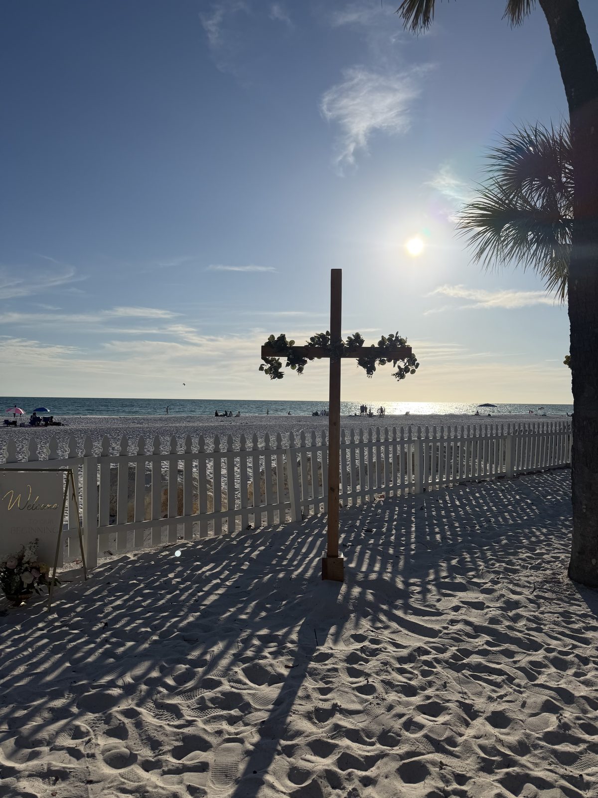 The cross set up beside the welcome sign, palm shadows across the sand