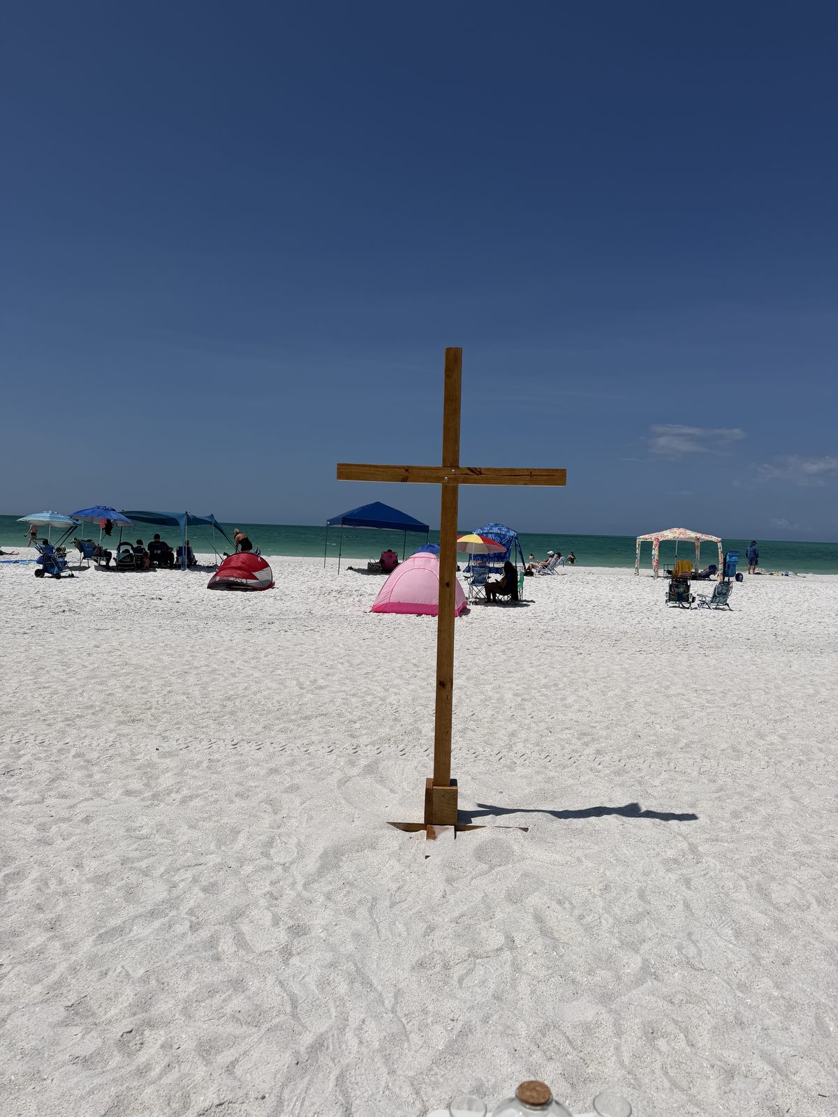 The bare stained cross planted in white sand against the Gulf
